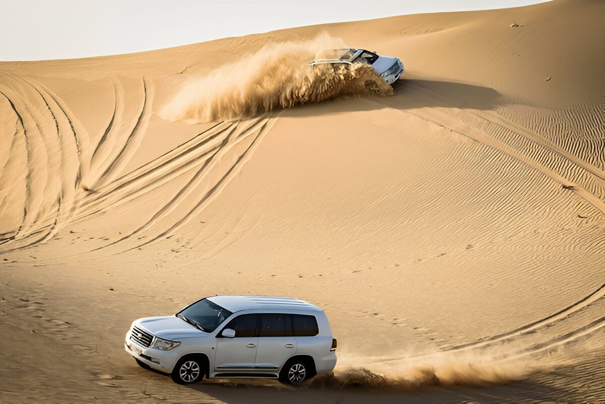 Thrilling scene of expert dune bashing drivers navigating steep sand dunes in 4x4 SUVs, kicking up clouds of sand under a clear blue sky." @exploredesertsafari.com