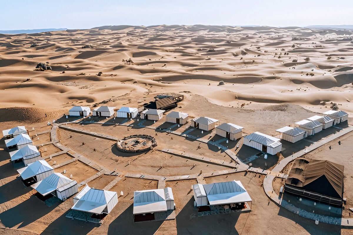 Luxurious Bedouin-style camp in the Dubai desert with a large elegant tent, rich carpets, plush cushions, and a gourmet dining setup under a starry night sky." @exploredesertsafari.com