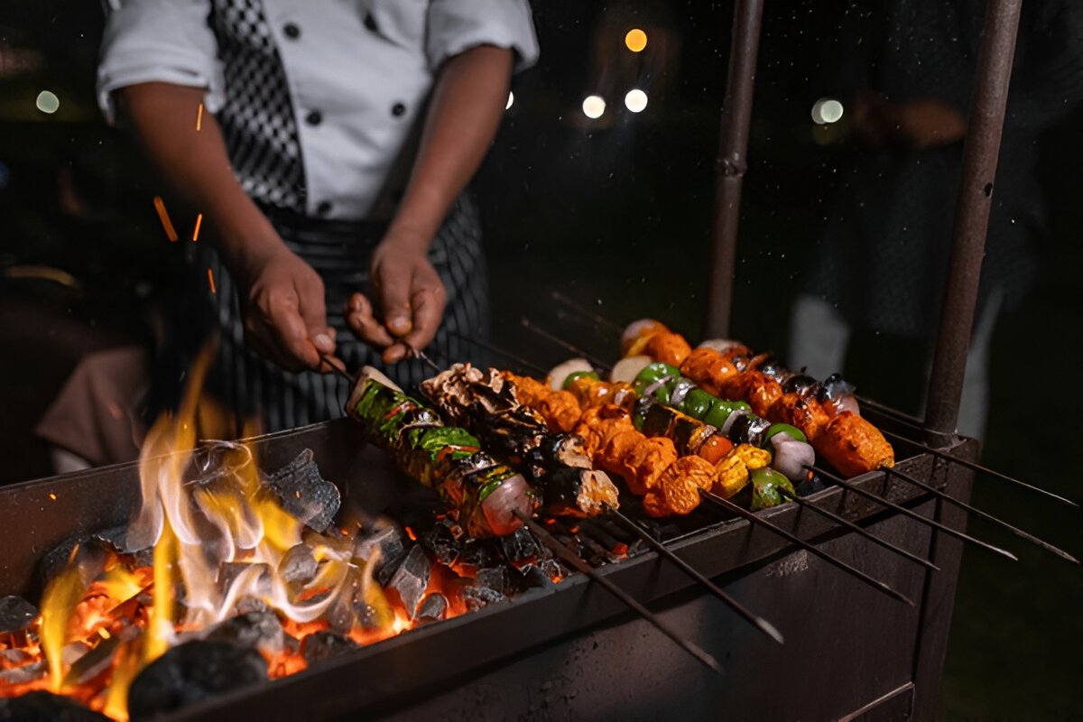 Stunning BBQ dinner buffet under the stars in the Dubai desert with gourmet dishes, plush seating, and lanterns illuminating the dining area surrounded by sand dunes." @exploredesertsafari.com