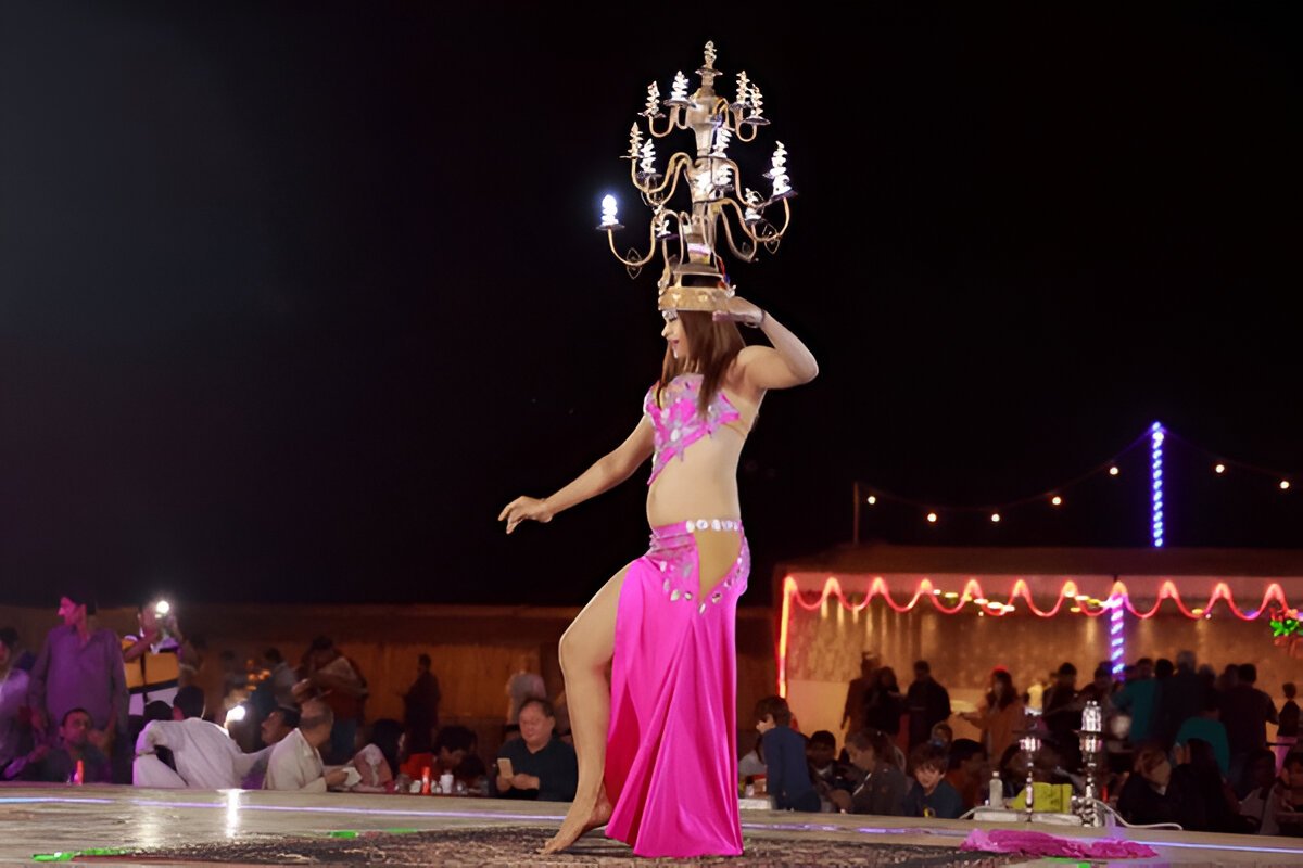 Vibrant belly dance performance in the Dubai desert, with the dancer in colorful attire and an audience seated under a starry sky." @exploredesertsafari.com