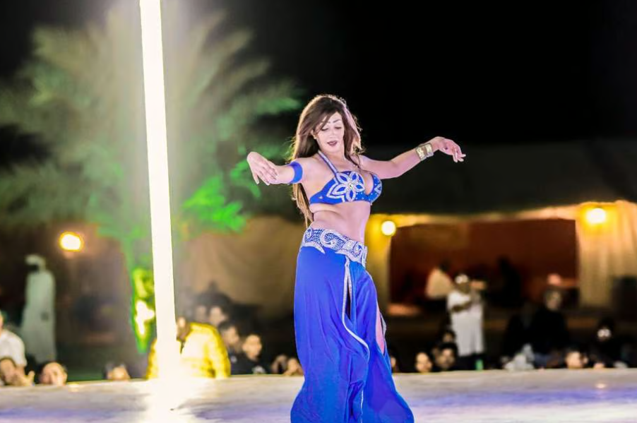 Vibrant belly dance performance in the Dubai desert, with the dancer in colorful attire and an audience seated under a starry sky." @exploredesertsafari.com